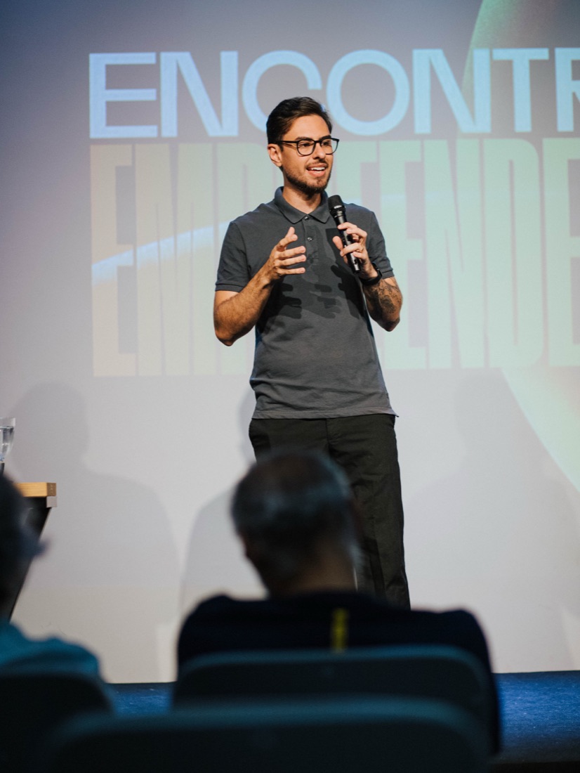 Guilherme Artesanos falando ao microfone em um palco